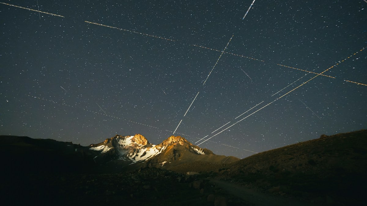 Long exposure light trails crossing a starry night sky above a snow-capped mountain